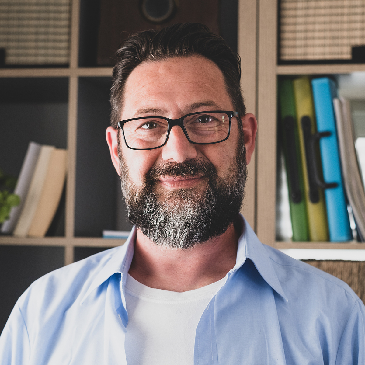 Close up of confident man in home with bookshelf behind him