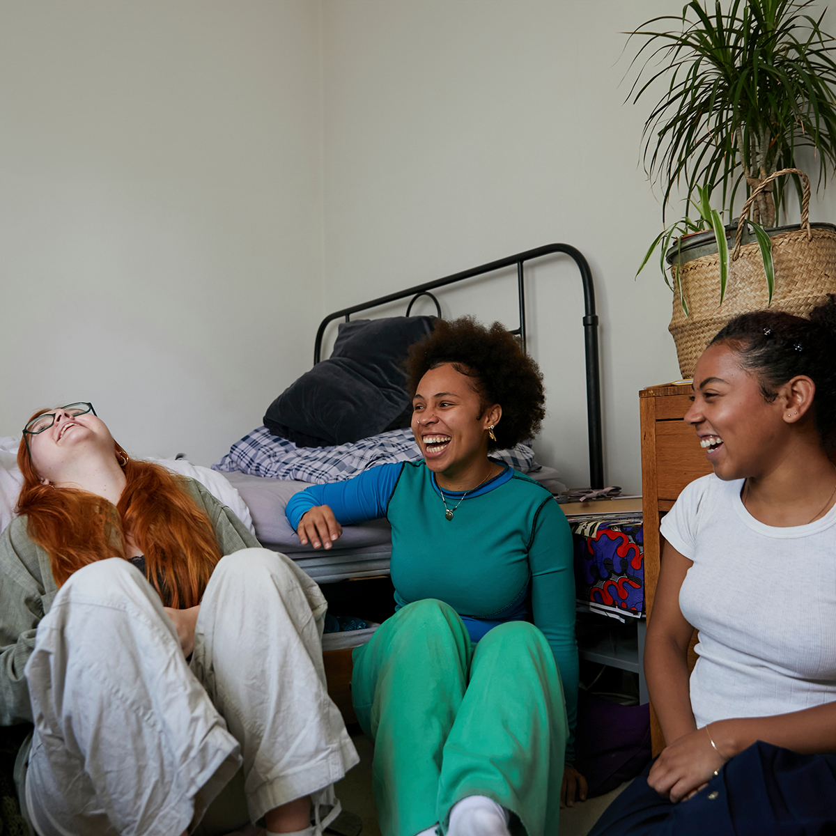 Three women sitting on the floor of a bedroom laughing together living in community